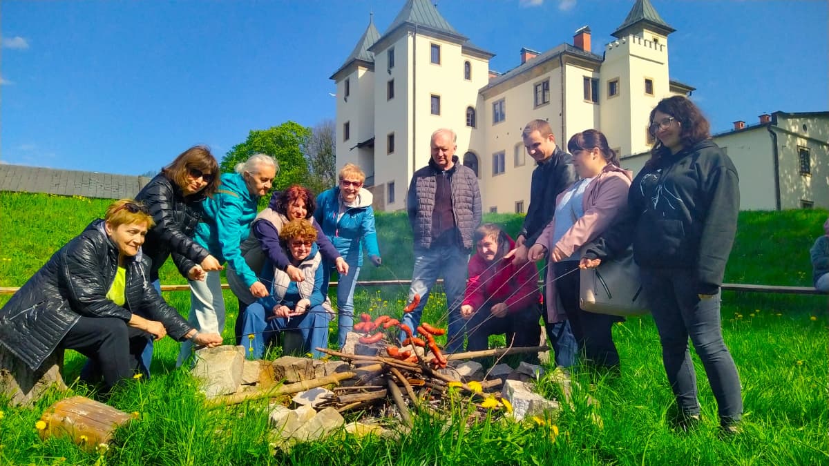 Grupa Niepokonanych piecze kiełbaski nad ogniskiem na tle zamku