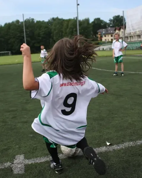 Chłopiec kopie piłkę na trawiastym boisku